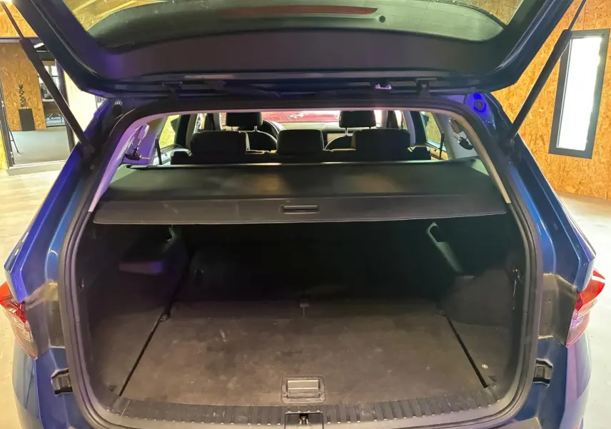 Coffre ouvert d’un Skoda Kodiaq bleu 2023, vue arrière montrant l’espace de chargement avec cache-bagages déployé.