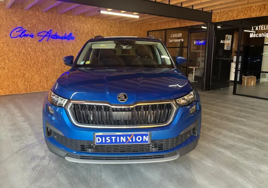 Vue avant d'un Skoda Kodiaq bleu 2023, mettant en valeur la calandre noire et les phares LED dans un showroom.