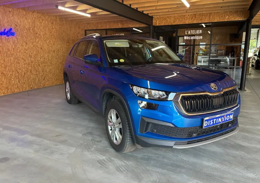 Vue 3/4 avant d'un Skoda Kodiaq bleu 2023 avec calandre noire et jantes argentées, stationné en intérieur.