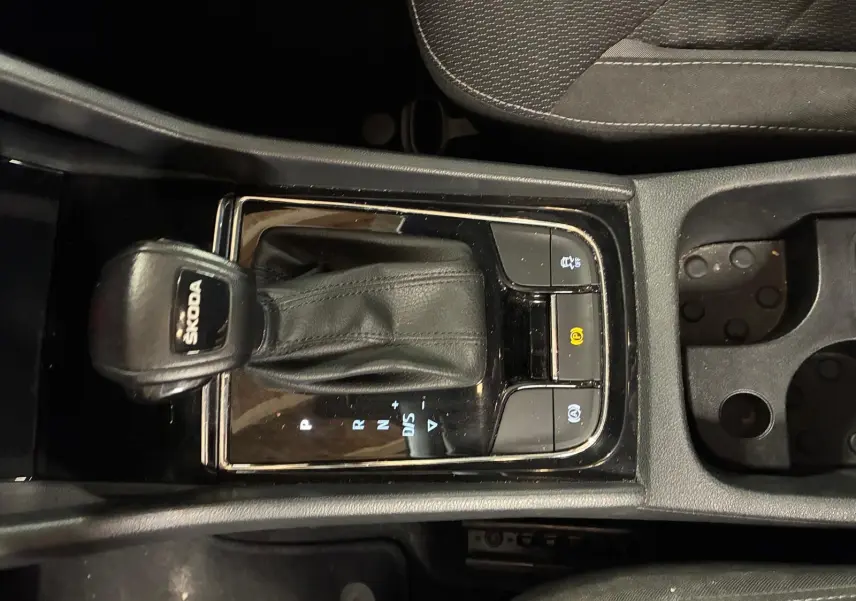 Vue rapprochée du levier de vitesses automatique noir marqué SKODA, entouré de boutons de commande, intérieur tissu noir.