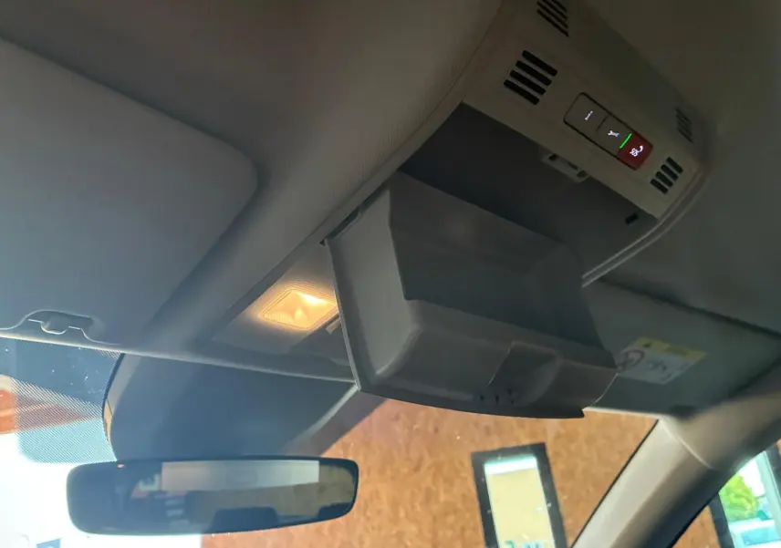 Vue intérieure du plafond avant d'un Skoda Kodiaq bleu 2023, avec rangement lunettes ouvert et éclairage allumé.