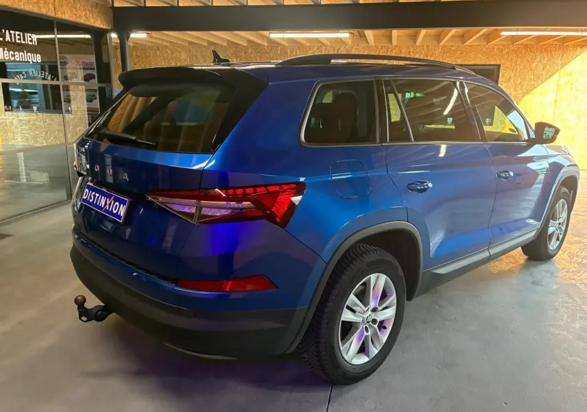 Vue 3/4 arrière droite d'un Skoda Kodiaq bleu 2023 avec attelage et vitres teintées, stationné en intérieur.