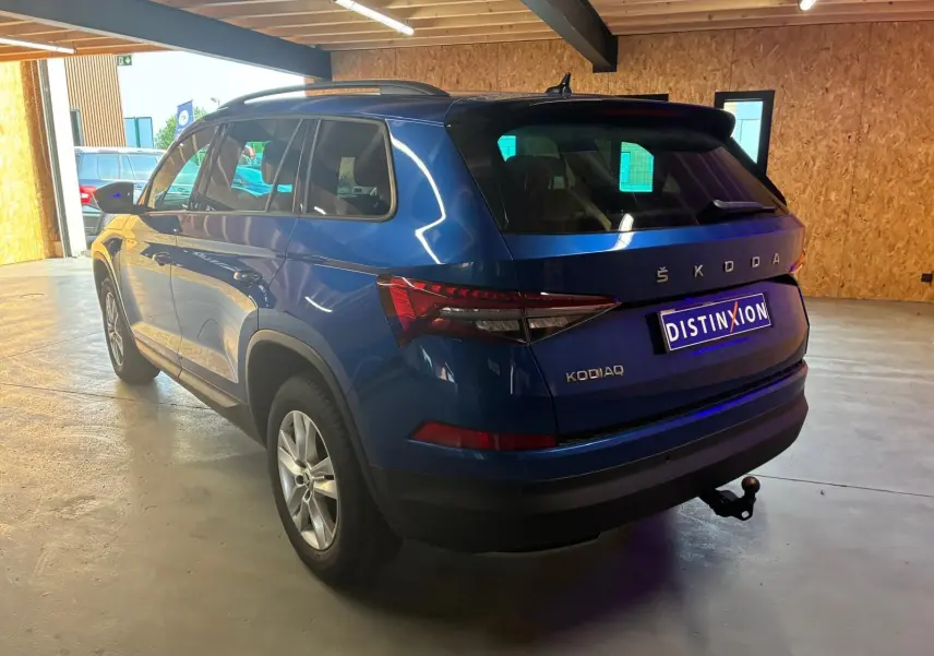 Vue 3/4 arrière droite d'un Skoda Kodiaq bleu 2023 avec attelage de remorque, dans un garage lumineux.