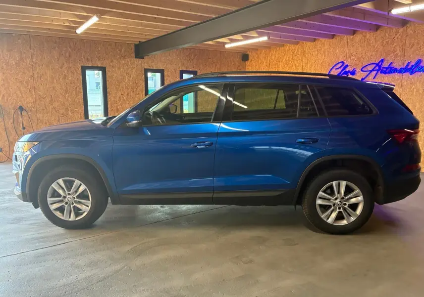 Vue de profil côté gauche d'un Skoda Kodiaq bleu 2023 stationné en intérieur avec jantes alliage et vitres teintées.