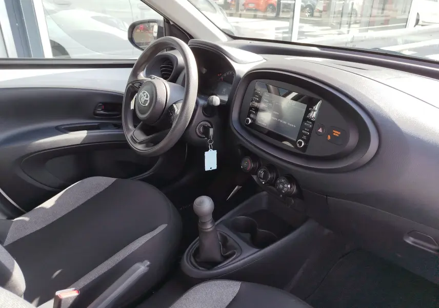 Intérieur de la Toyota Aygo X blanc pur, vue côté conducteur, tableau de bord avec écran tactile et boîte manuelle.