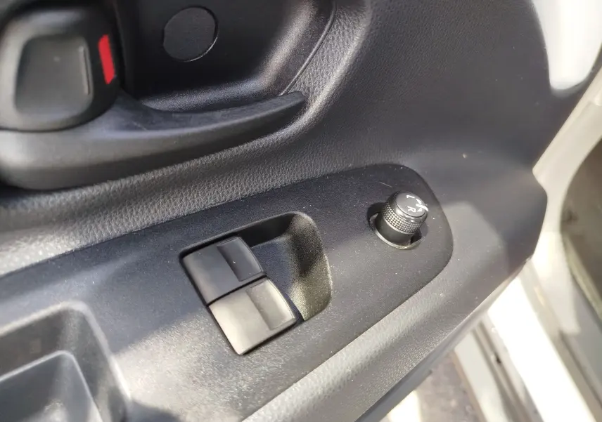 Gros plan sur la commande de réglage des rétroviseurs et les boutons de lève-vitres côté conducteur d'une Toyota Aygo X blanc pur.