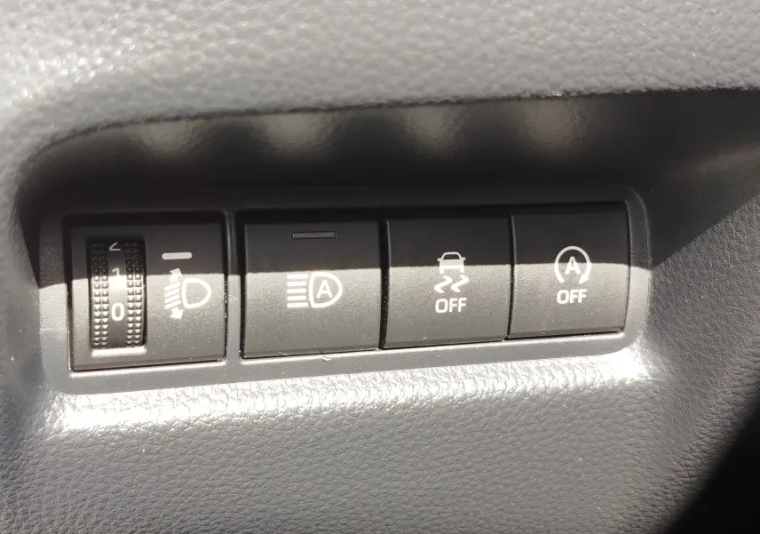 Gros plan sur les commandes de réglage des phares et des aides à la conduite dans une Toyota Aygo X blanche.