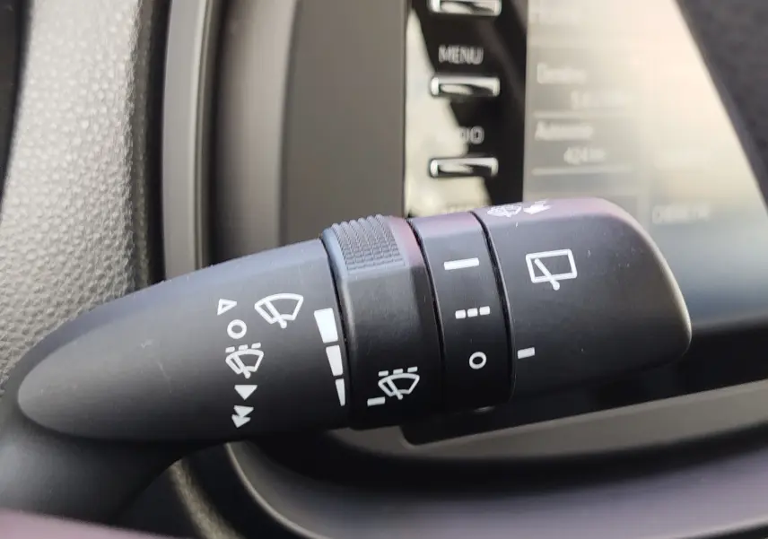 Gros plan sur la manette de commande des essuie-glaces dans l'habitacle d'une Toyota Aygo X blanche, détails des symboles visibles.