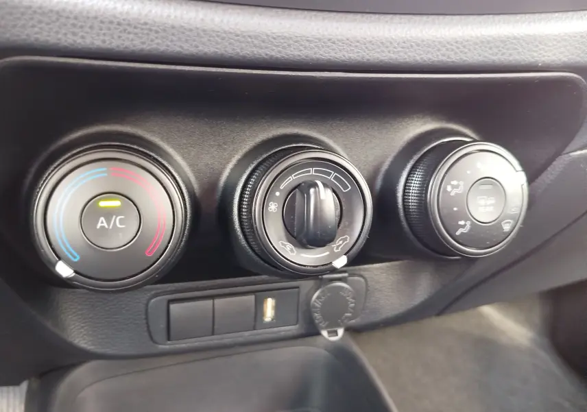 Gros plan sur les commandes de climatisation manuelle noires de la Toyota Aygo X blanche, avec réglage température, ventilation et désembuage.