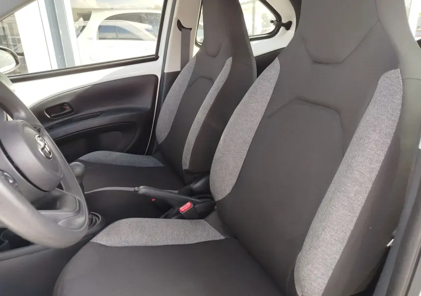 Vue intérieure côté gauche de la Toyota Aygo X 2023, sièges tissu bicolore noir et gris, volant multifonction visible.