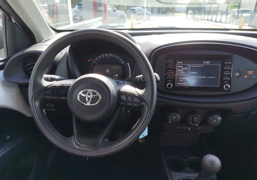 Vue intérieure centrée sur le volant Toyota et le tableau de bord avec écran tactile et commandes manuelles.