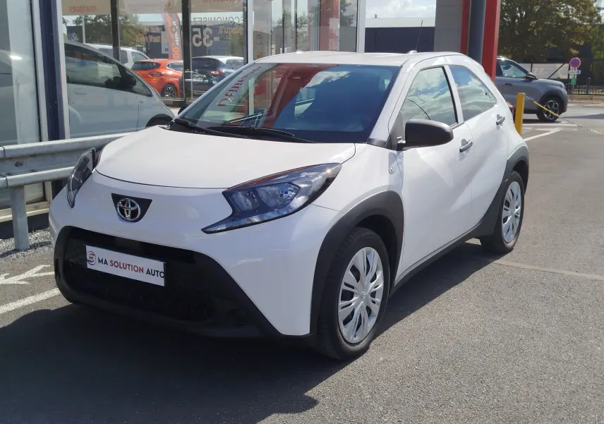 Toyota Aygo X blanc pur vue 3/4 avant droit, avec boucliers noirs contrastants et jantes compactes.