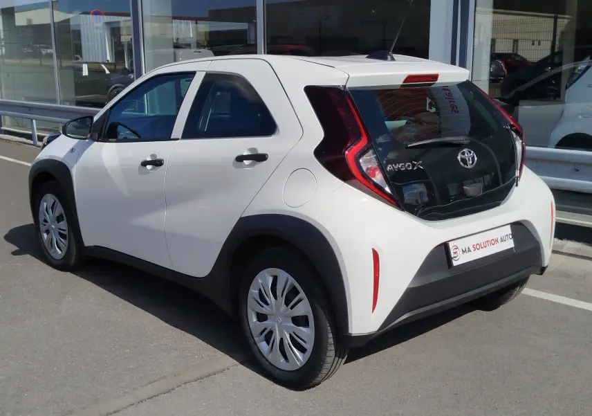 Toyota Aygo X blanche vue 3/4 arrière droit, avec hayon noir contrastant et feux arrière en forme de C.