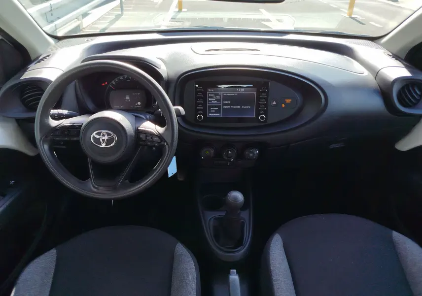 Vue intérieure avant de la Toyota Aygo X blanche, montrant le volant, tableau de bord et écran central tactile.