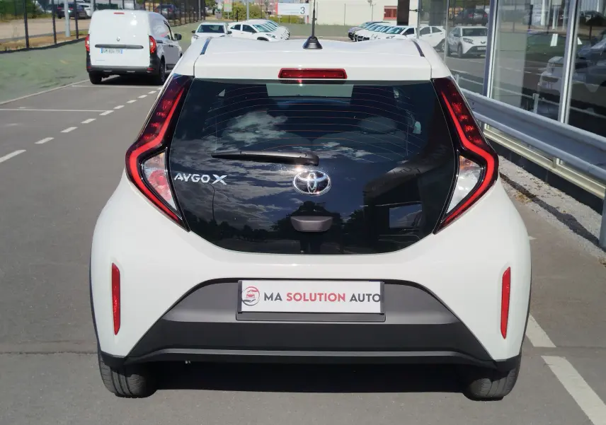 Vue arrière d'une Toyota Aygo X blanche Pure 2023 avec hayon noir brillant et feux arrière en forme de boomerang.