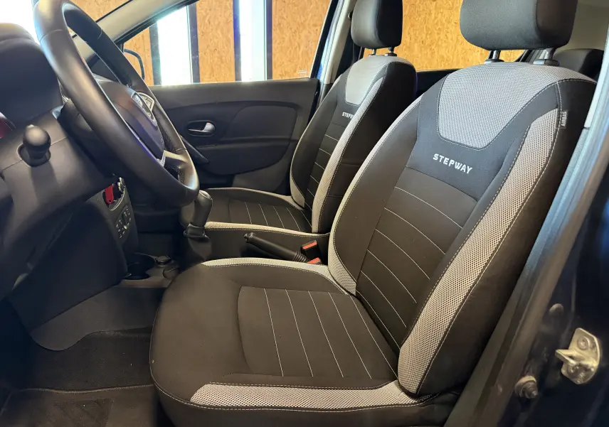 Vue intérieure côté conducteur de la Dacia Sandero Stepway 2019 bleu, sièges noirs avec logo Stepway brodé.