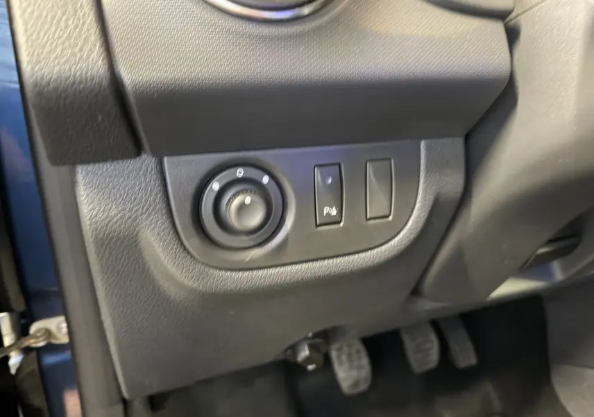 Détail intérieur côté gauche du tableau de bord d'une Dacia Sandero Stepway bleu 2019, avec commandes de réglage et pédales visibles.