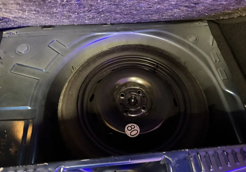 Roue de secours noire dans le coffre d'une Dacia Sandero Stepway bleu 2019, vue plongeante sur le pneu.