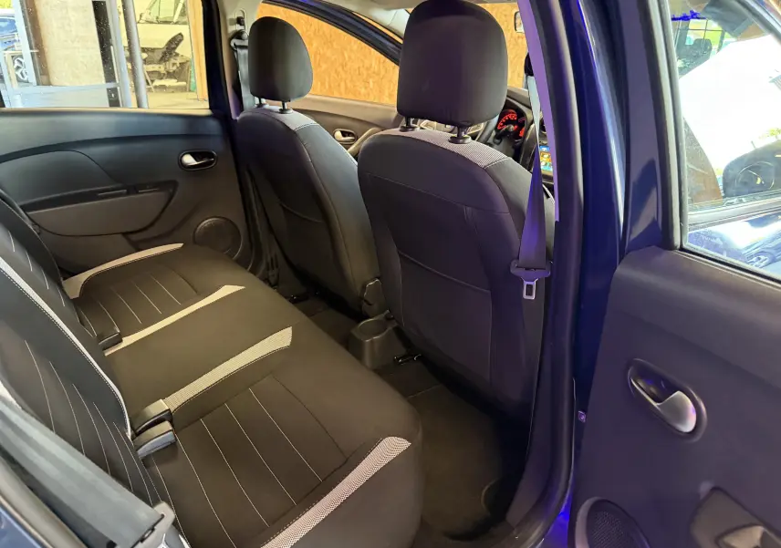 Vue intérieure arrière côté droit d'une Dacia Sandero Stepway bleu, montrant les sièges noirs avec inserts gris et ceintures de sécurité.