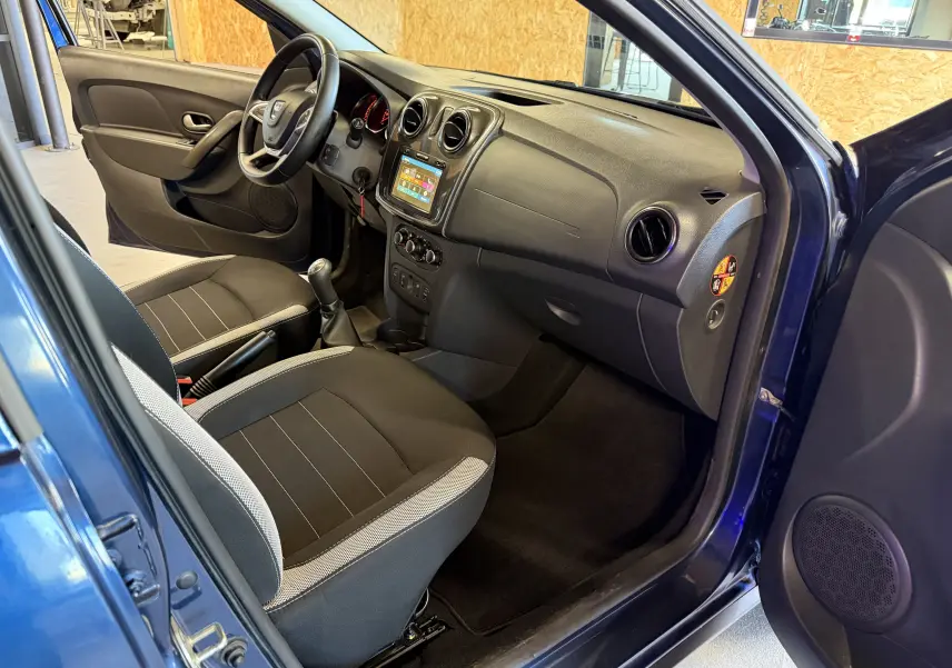 Intérieur côté conducteur d'une Dacia Sandero Stepway bleu 2019, montrant tableau de bord et sièges noirs avec console centrale.
