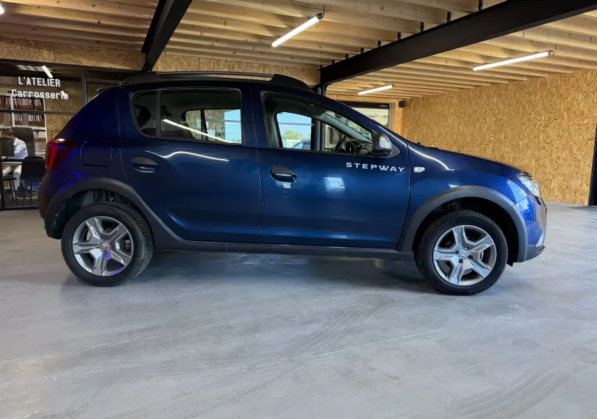 Vue de profil côté gauche d'une Dacia Sandero Stepway bleu foncé avec logo Stepway visible sur la porte avant.