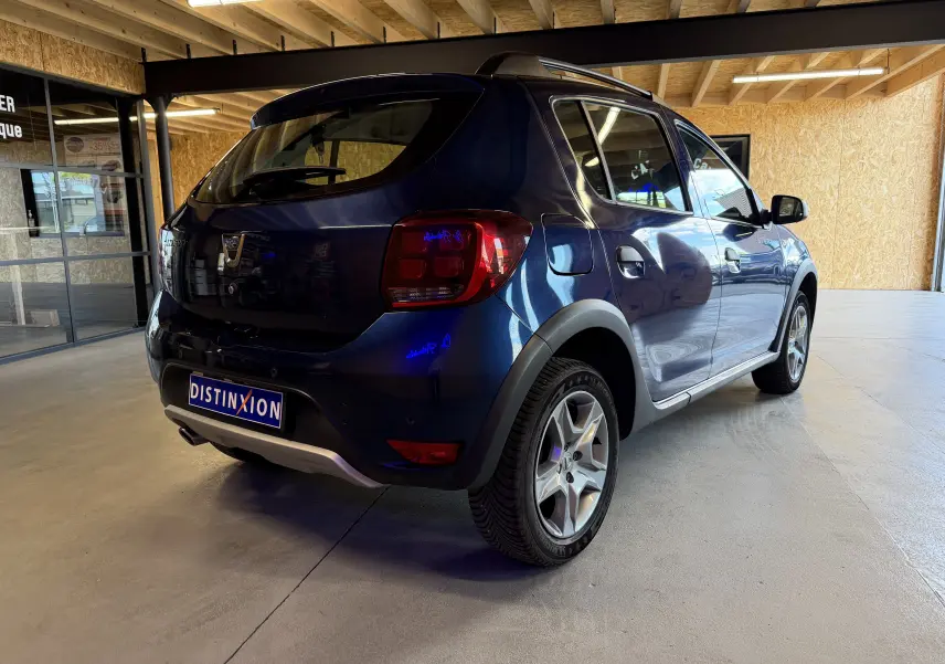 Vue 3/4 arrière droite d'une Dacia Sandero Stepway bleu foncé 2019, avec protections plastiques noires et jantes alliage.