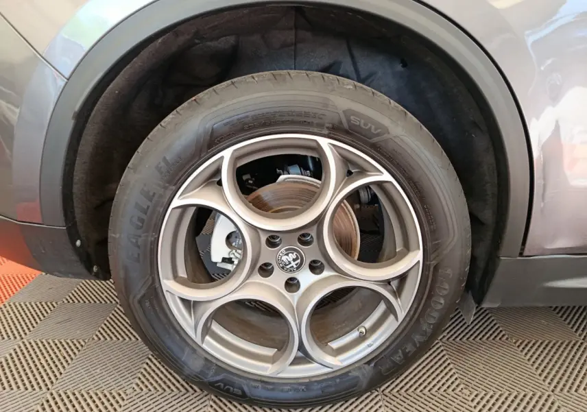 Gros plan sur la roue avant gauche gris foncé d’un Alfa Romeo Stelvio 2024 avec jante en alliage à cinq cercles entrelacés.
