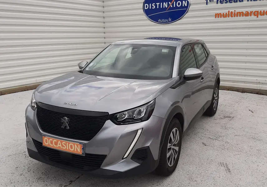 Peugeot 2008 gris Artense vue 3/4 avant droit, avec calandre noire et phares LED, stationnée devant un mur blanc.