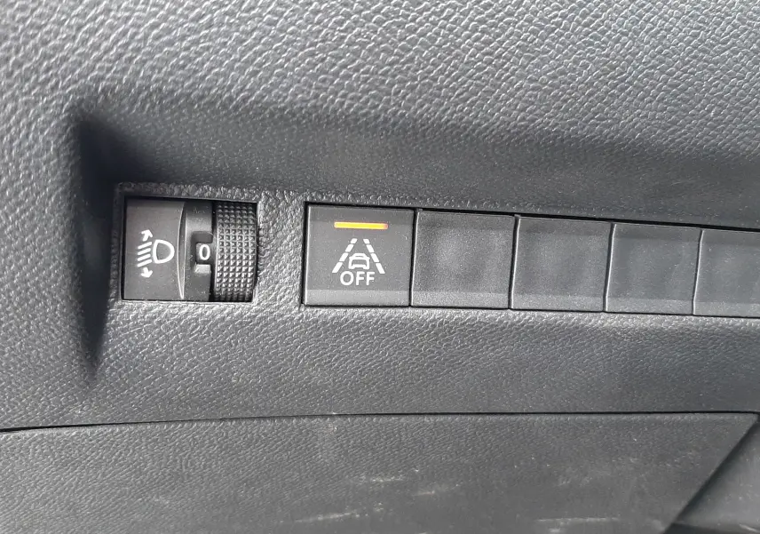 Gros plan sur les commandes de réglage des phares et de désactivation de l'alerte de franchissement de ligne dans un Peugeot 2008 gris Artense.