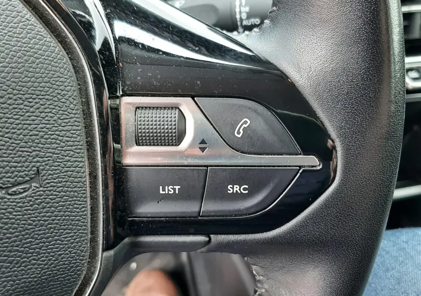Gros plan sur les commandes au volant côté gauche du Peugeot 2008 gris Artense, avec boutons LIST, SRC et téléphone.