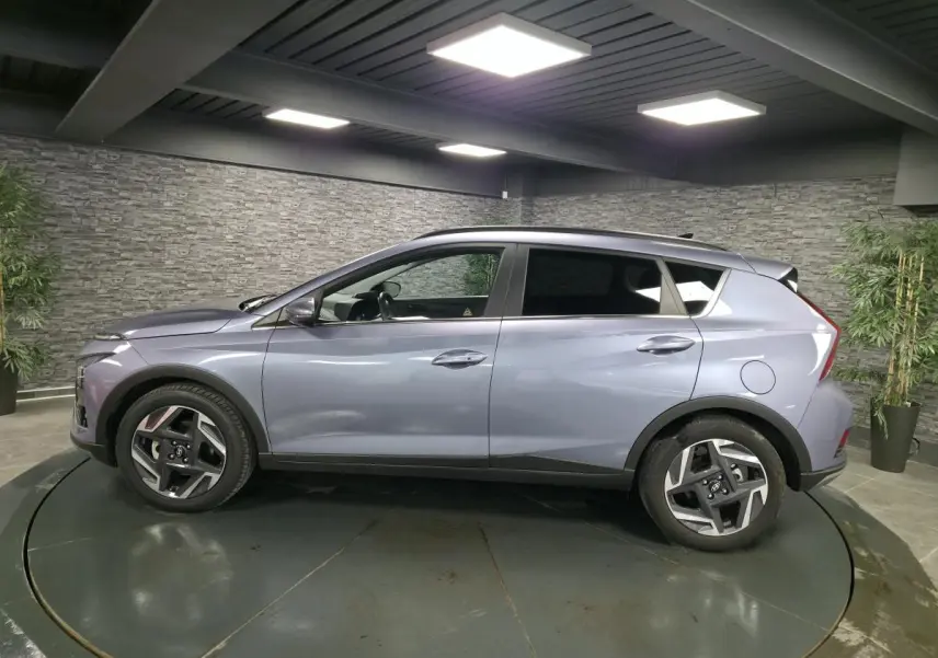 Vue de profil côté gauche d’un Hyundai Bayon gris métallisé avec jantes alliage 17 pouces dans un showroom.