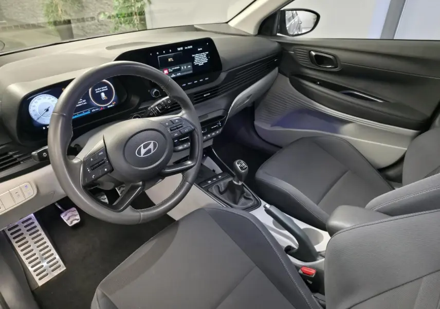 Vue intérieure côté conducteur du Hyundai Bayon 2025 gris, avec volant cuir, tableau de bord numérique et boîte manuelle.