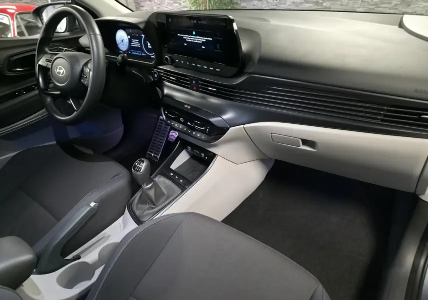Vue intérieure côté conducteur du Hyundai Bayon 2025, tableau de bord bi-ton gris et noir avec écran tactile et levier de vitesses manuel.