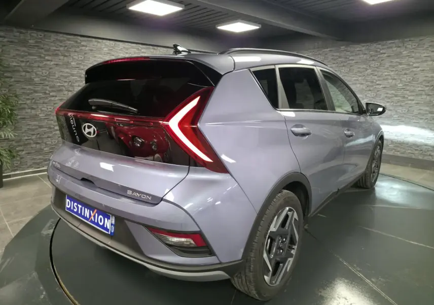 Vue 3/4 arrière droite d'une Hyundai Bayon gris métallisé avec feux arrière LED en forme de flèche et jantes alliage 17 pouces.