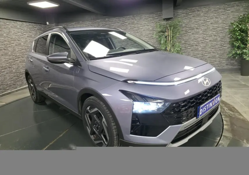 Hyundai Bayon gris métallisé vue 3/4 avant droit avec calandre noire laquée et feux LED allumés.