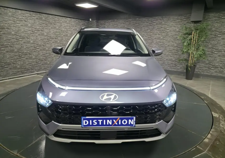 Vue avant d'une Hyundai Bayon gris métallisé avec calandre noire laquée et feux LED allumés dans un showroom.