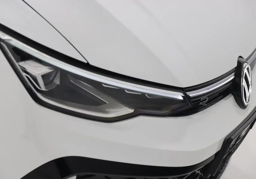 Gros plan sur le phare avant gauche blanc d’une Volkswagen Golf 2.0 TDI R-Line avec logo VW et bande LED.