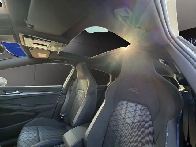 Vue intérieure de la Volkswagen Golf 2.0 TDI R-Line 2025, sièges sport noirs et toit panoramique ouvert avec lumière naturelle.