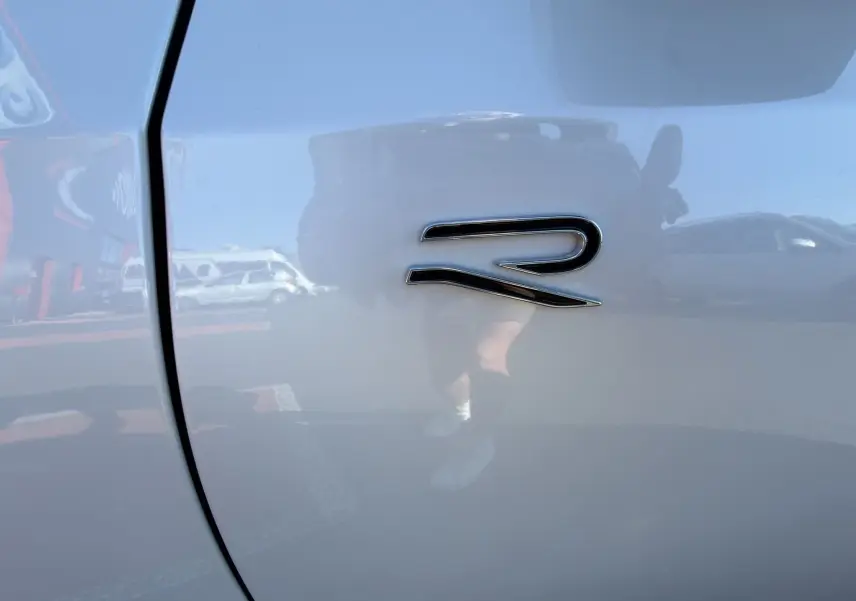 Gros plan sur l'emblème "R" noir brillant sur la carrosserie blanche d'une Volkswagen Golf 2.0 TDI R-Line.