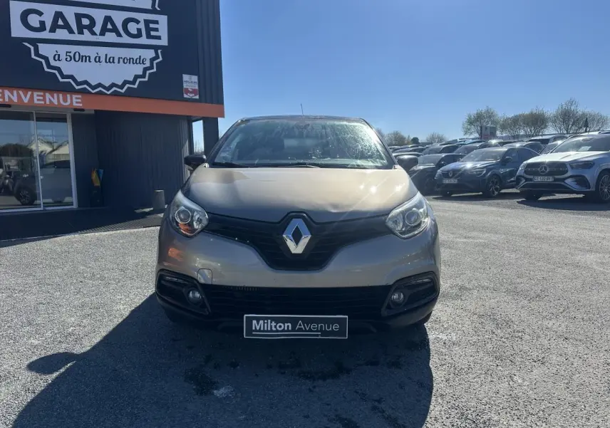 Vue avant d'un Renault Captur beige métallisé 2014, avec calandre noire et phares arrondis sous un ciel dégagé.