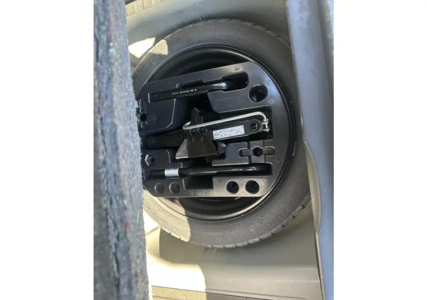 Vue rapprochée de la roue de secours galette et outils dans le coffre d’un Renault Captur beige 2014.