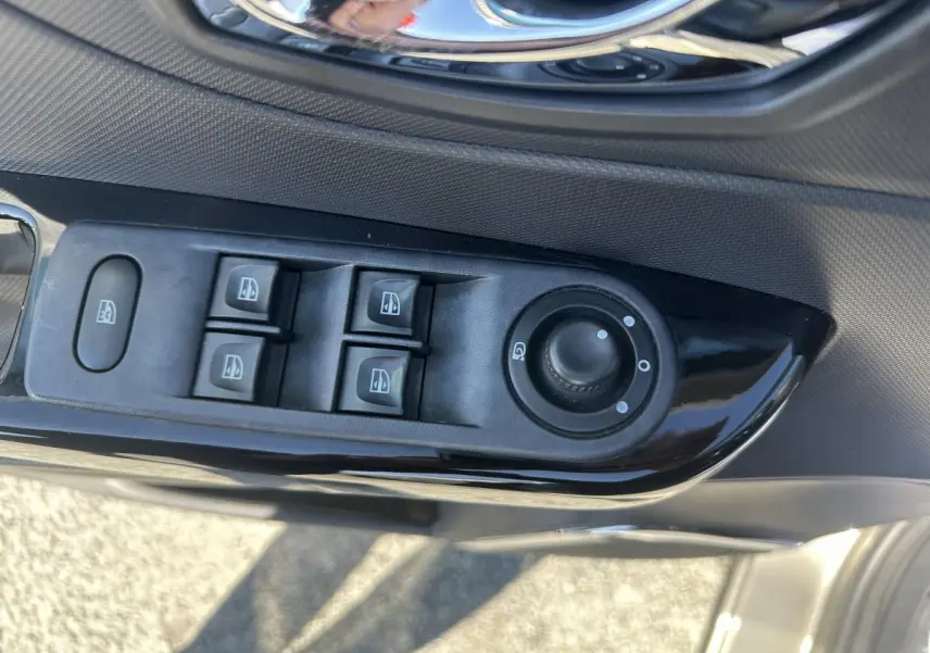 Gros plan sur les commandes de lève-vitres et réglage des rétroviseurs côté conducteur du Renault Captur beige.