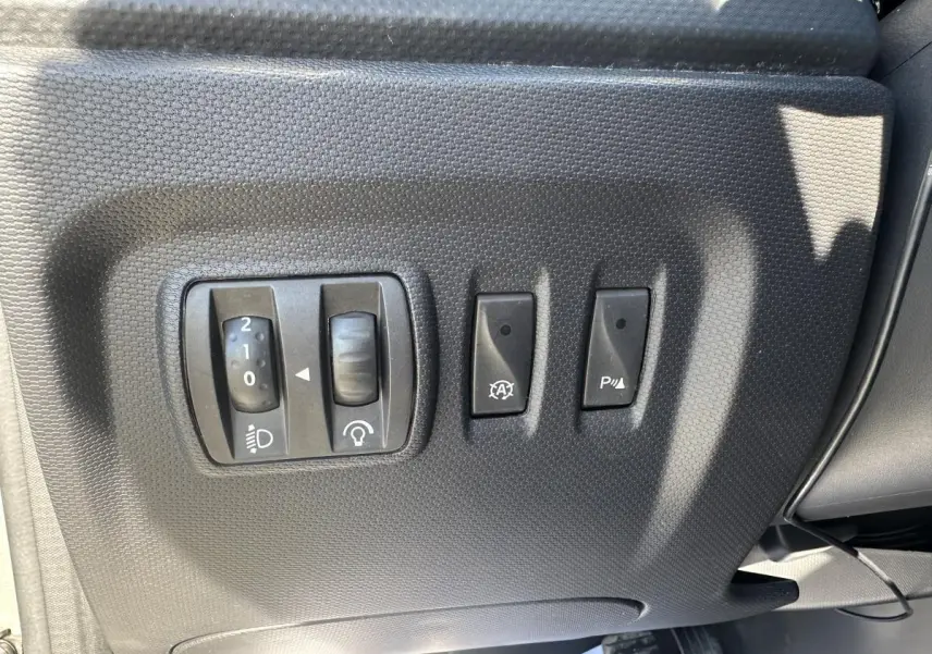 Gros plan sur les commandes de réglage des phares et aides à la conduite côté conducteur du Renault Captur beige 2014.