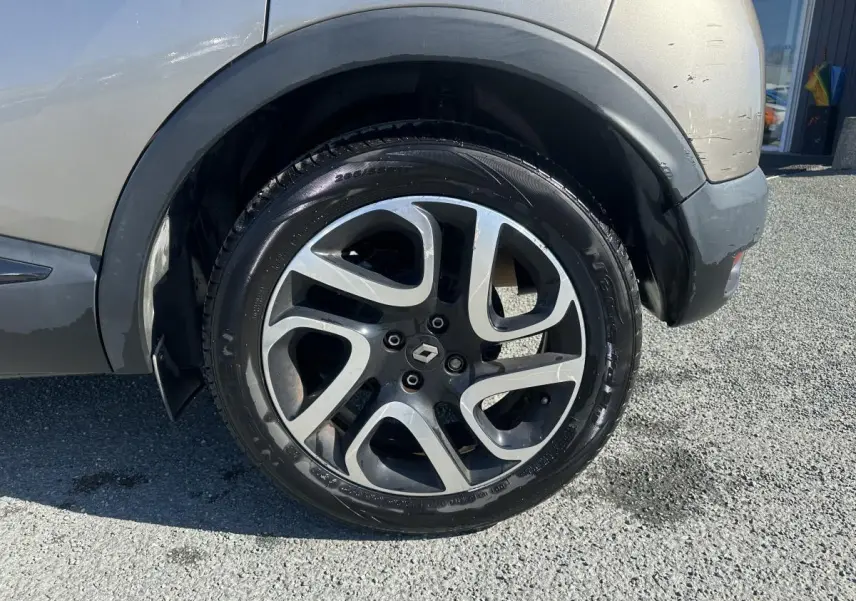 Gros plan sur la roue arrière droite du Renault Captur beige, jante alliage noir diamanté avec logo Renault central.