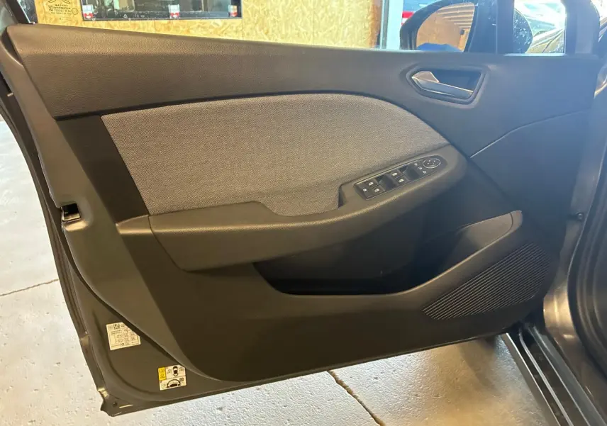 Vue intérieure côté gauche de la porte avant d'une Renault Clio gris schiste avec commandes des vitres et tissu gris.