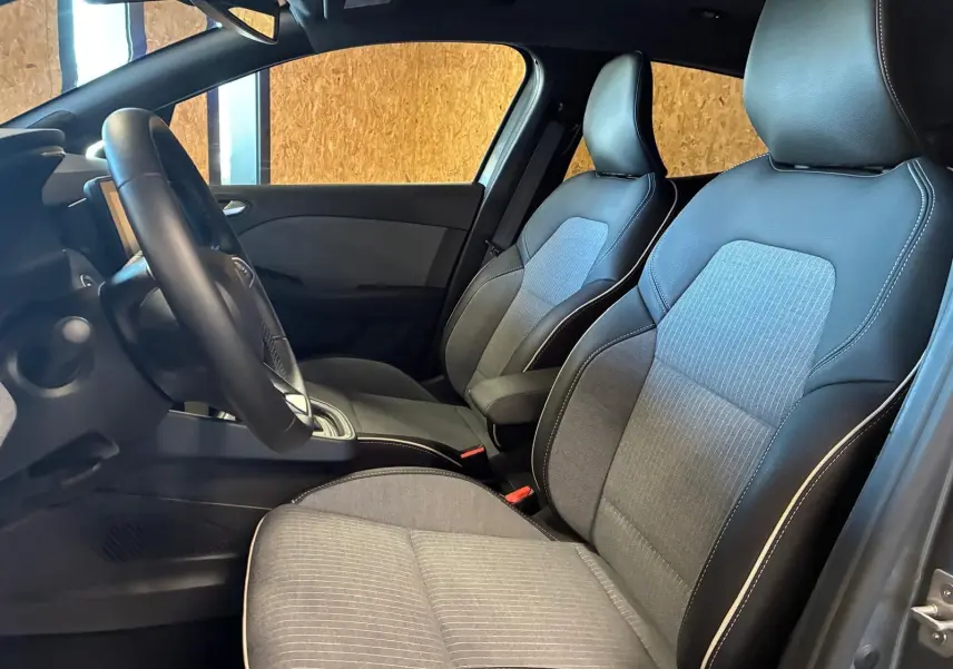 Vue intérieure côté conducteur de la Renault Clio 2025, sièges tissu gris clair avec contours en cuir noir.