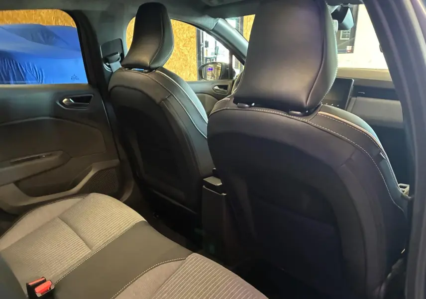Vue intérieure arrière de la Renault Clio 2025, sièges tissu gris noir avec surpiqûres blanches, ambiance sobre et moderne.