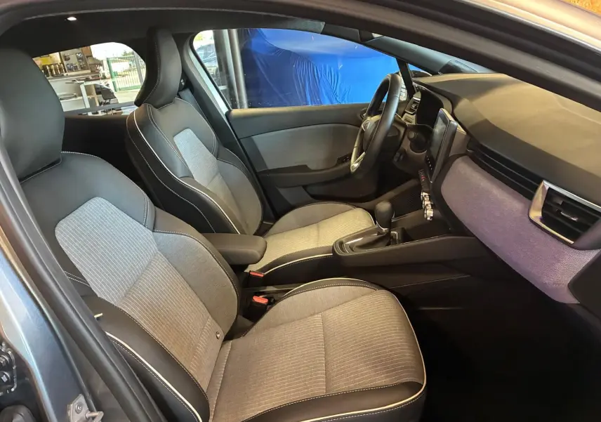 Intérieur de la Renault Clio 2025 en gris schiste, vue côté gauche sur les sièges tissu gris clair avec surpiqûres blanches.