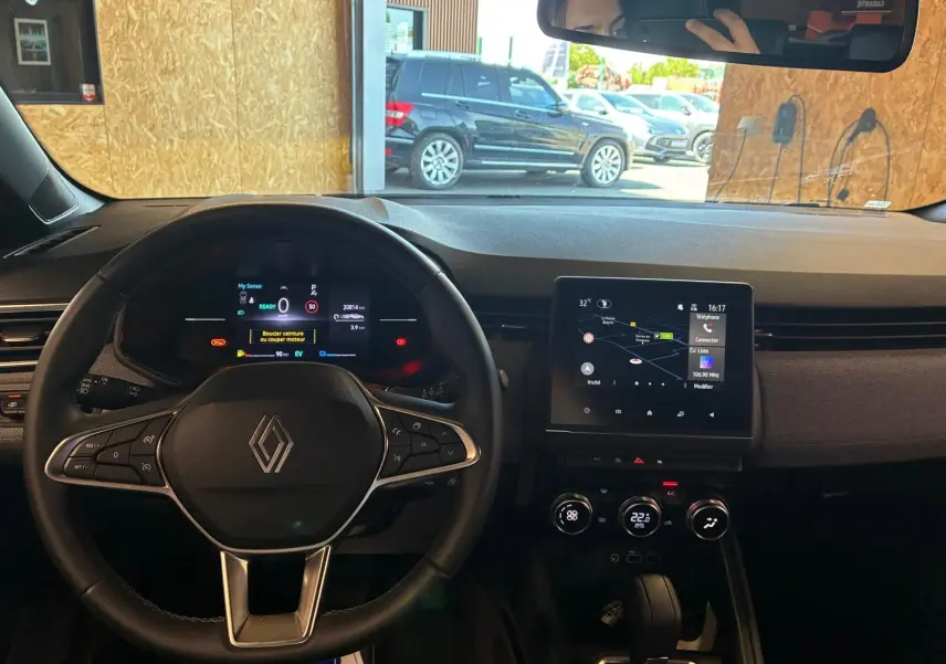 Vue intérieure centrée sur le volant et le tableau de bord numérique de la Renault Clio gris schiste avec écran tactile et commandes intégrées.