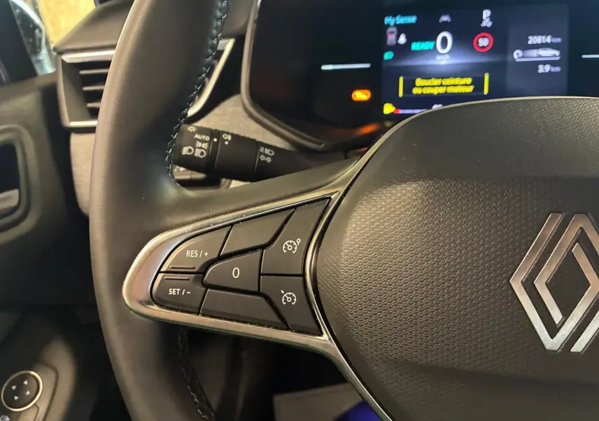 Gros plan sur le volant côté gauche de la Renault Clio gris schiste, avec commandes de régulateur de vitesse et tableau de bord numérique.